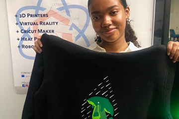 student holds up a tee shirt with a design added on with a heat press