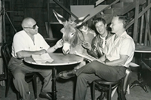 Men sitting around a card table with a donkey